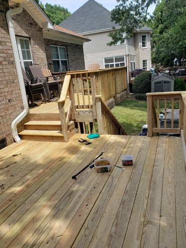 Newly built wooden deck with tools and stacked chairs nearby.
