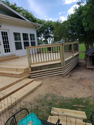 Newly built wooden deck with black railings attached to a white house.