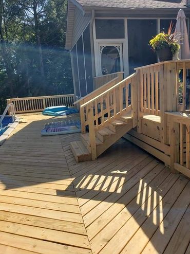 Spacious wooden deck with stairs leading to a screened porch and pool area.
