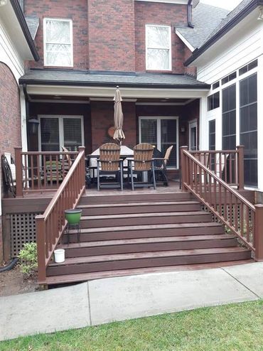 Wooden deck with stairs and outdoor dining set in a suburban backyard.