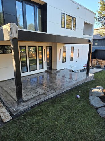 Modern patio with tiled flooring and black pillars under a white house extension.