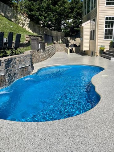 Curved blue backyard pool with stone waterfall near house patio.