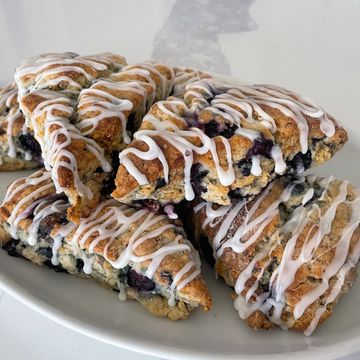 Blueberry scones drizzled with white icing on a white plate.