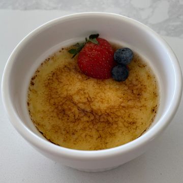 A ramekin of crème brûlée topped with a strawberry and two blueberries.