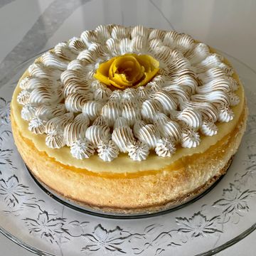 A beautifully decorated cheesecake with whipped cream and a yellow rose on top.