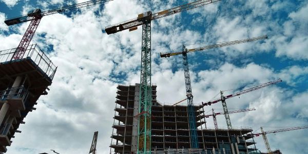 Construction cranes working on a building project under a blue sky.