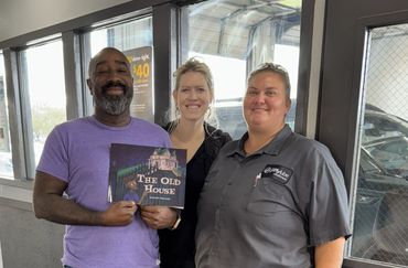 Three people smiling, one holding a book titled 'The Old House'.