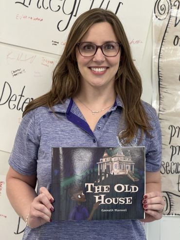 A smiling woman in glasses holds a book titled 'The Old House' by Kenneth Maxwell.