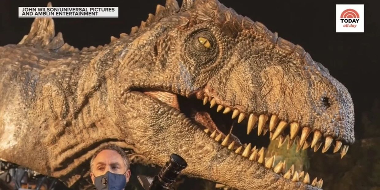 A man wearing a mask is standing next to a dinosaur.