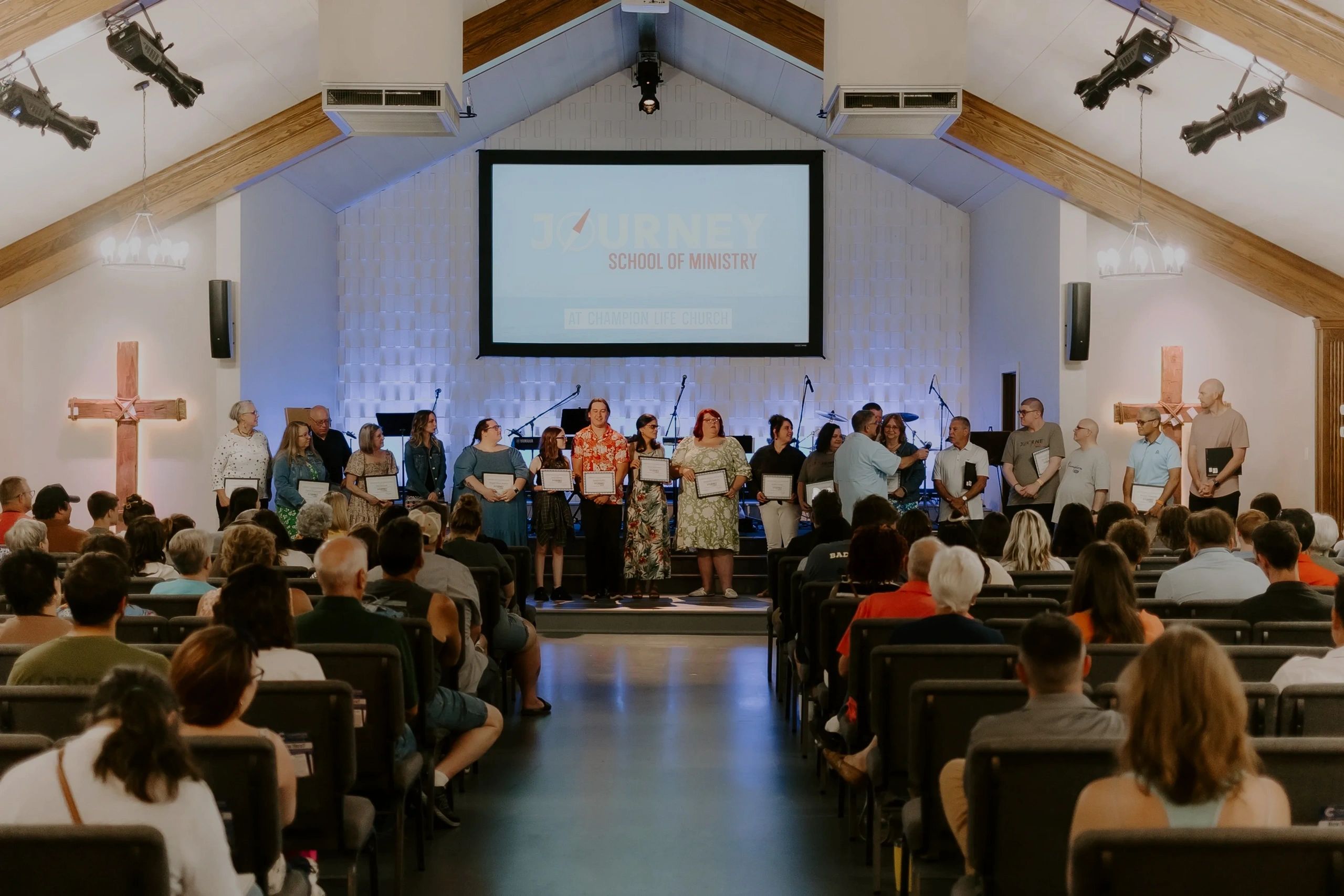 Recent grads of Journey stand on stage at Champion Life Church to recieve their certificates