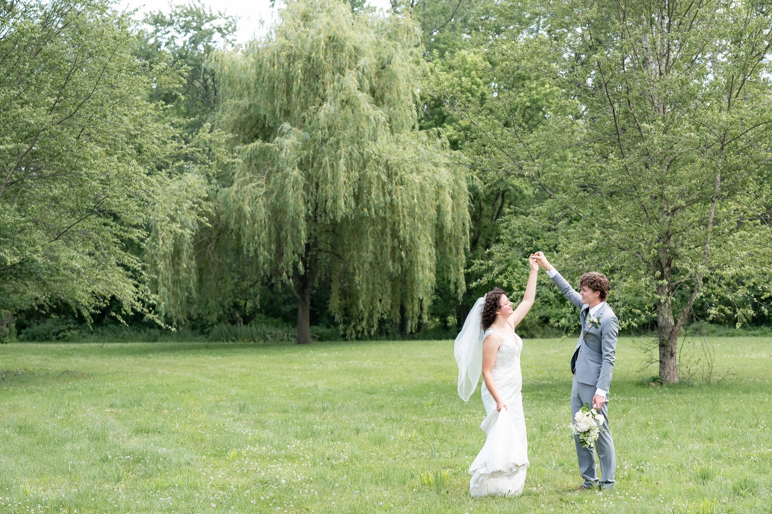 Bride and groom dancing outside surrounded by greenery.