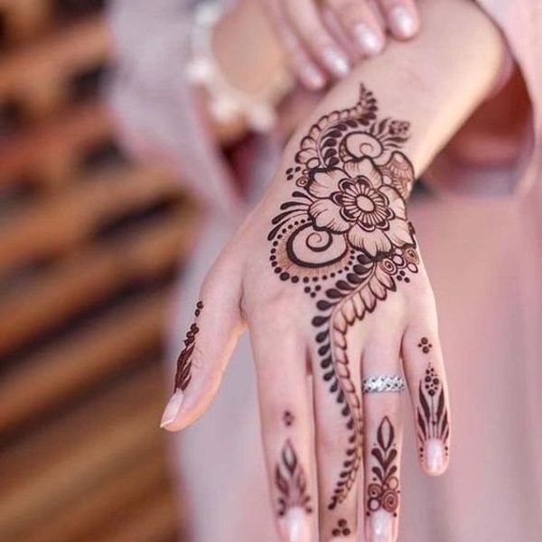 Intricate floral henna design on the back of a hand with a silver ring.