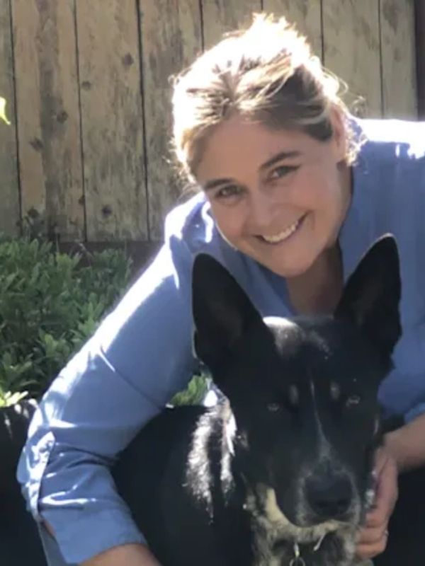 Woman smiling happily with a black dog outdoors.