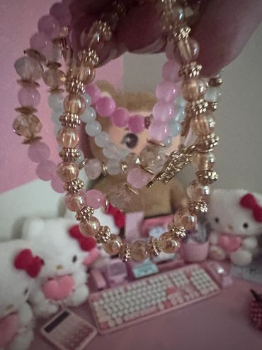 Beaded bracelets held in front of Hello Kitty plush and pink keyboard.