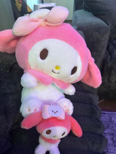 Two pink and white plush toys stacked on a gray couch.
