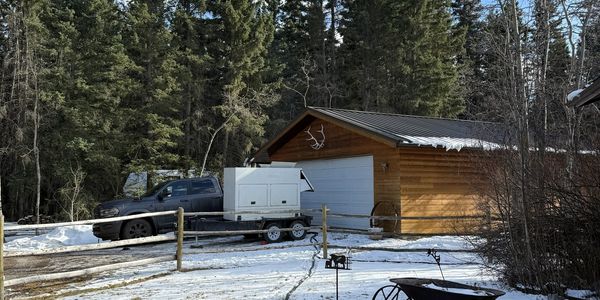 Black truck parked outside a wooden garage in a snowy forest area.