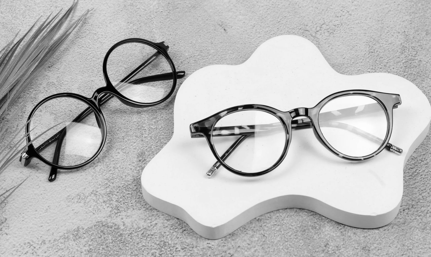 Two pairs of stylish eyeglasses on a textured surface and white decorative tray.