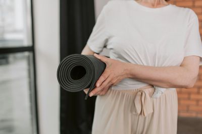 Person holding a rolled-up black yoga mat indoors.