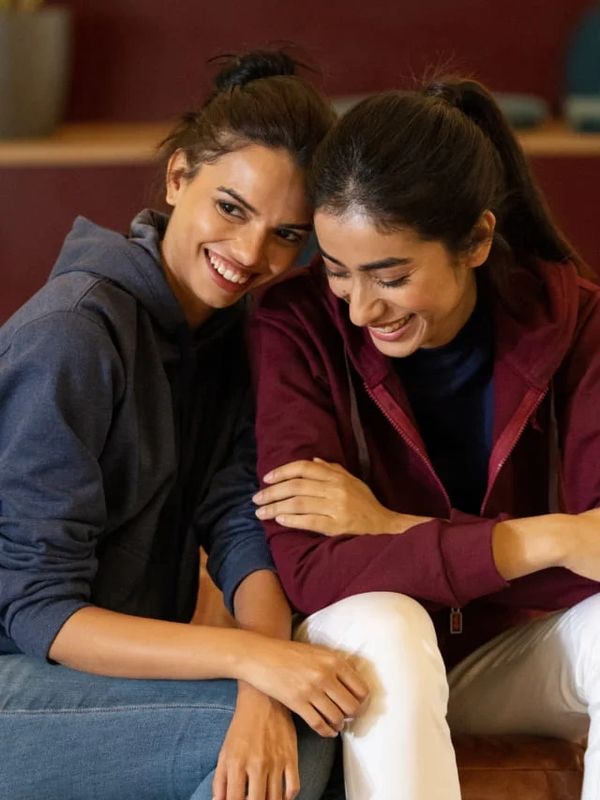 Two women smiling and leaning on each other joyfully.
