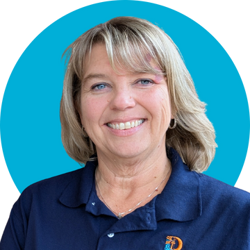 Smiling woman with blonde hair wearing a navy blue polo shirt against a blue background.