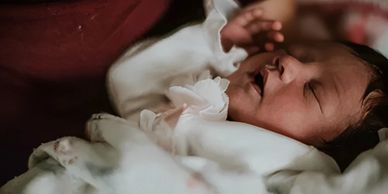 Newborn baby with hand by her face and eyes closed.