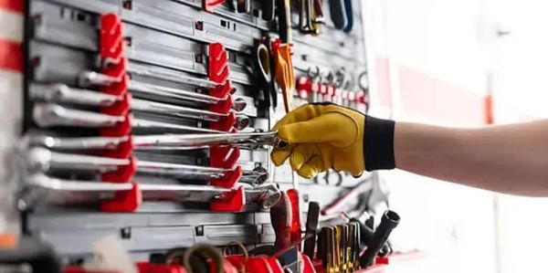 Hand with yellow glove selecting a wrench from a tool rack.
