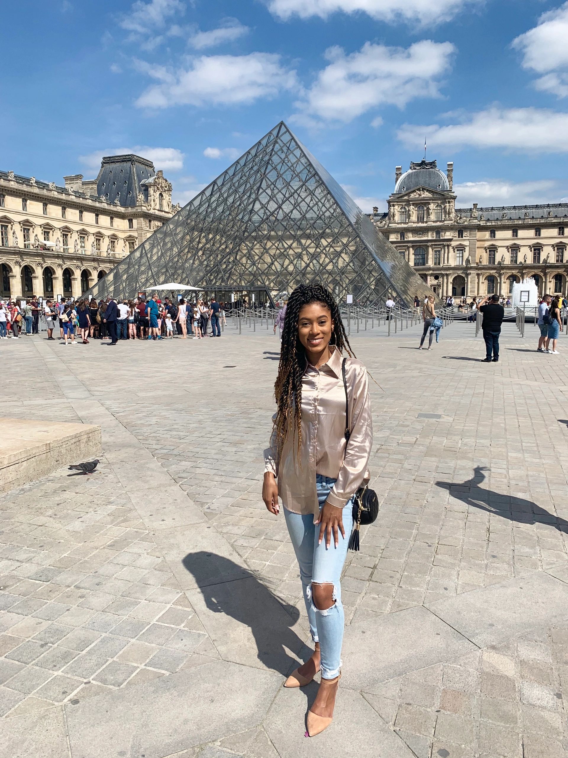 Smiling woman in front of the Louvre Pyramid in Paris.