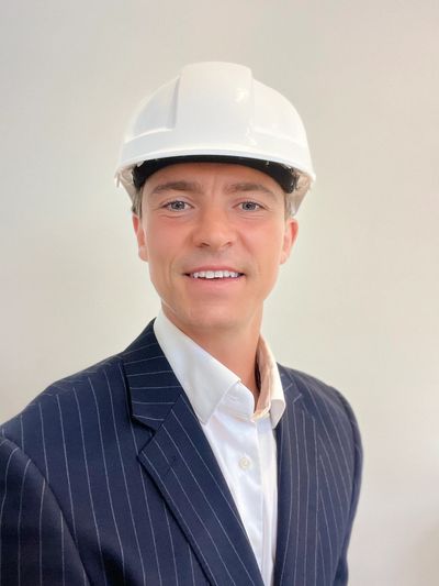 Man in suit and hard hat smiling.