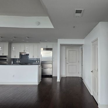Modern apartment kitchen with dark wooden floors and white cabinets.