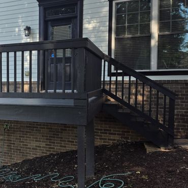 Freshly painted black wooden deck attached to a house with stairs.