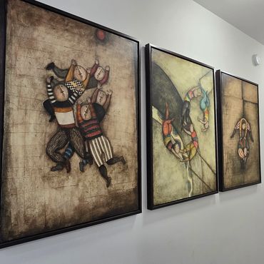 Three framed abstract paintings with whimsical figures on a white hallway wall.