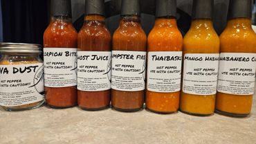A variety of homemade hot pepper sauces and dusts lined up on a counter.
