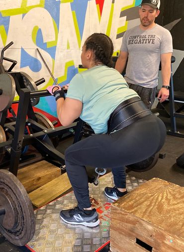 Client performing a belt squat in gym under trainer supervision.