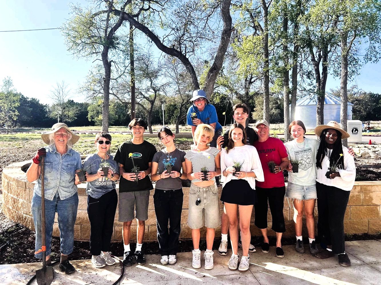 Group of people holding plants outdoors, smiling and posing for a photo.