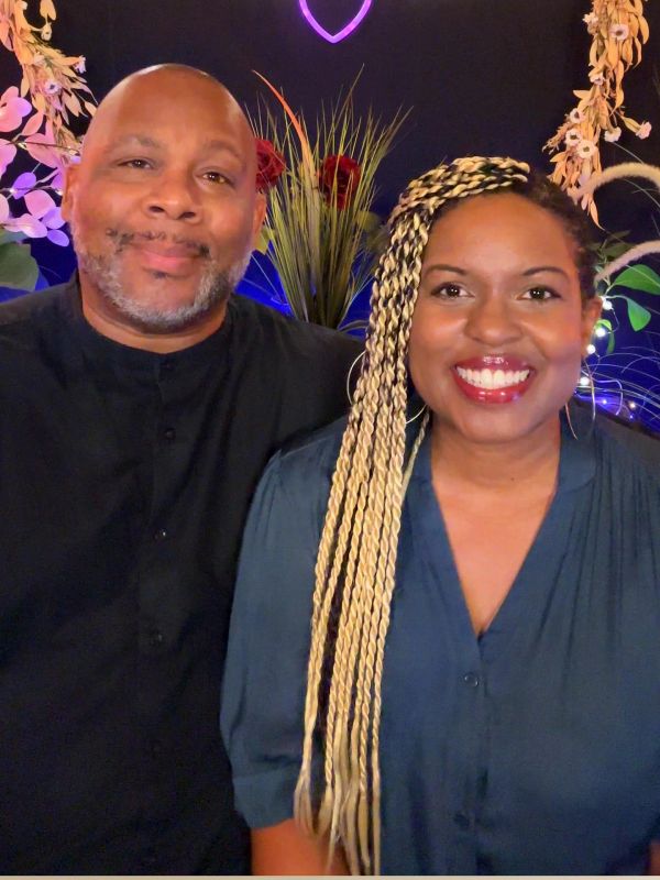 Smiling couple posing in front of decorative plants and lights.