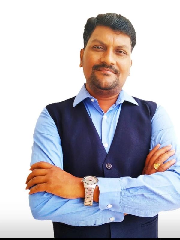 Man in blue shirt and black vest with crossed arms.