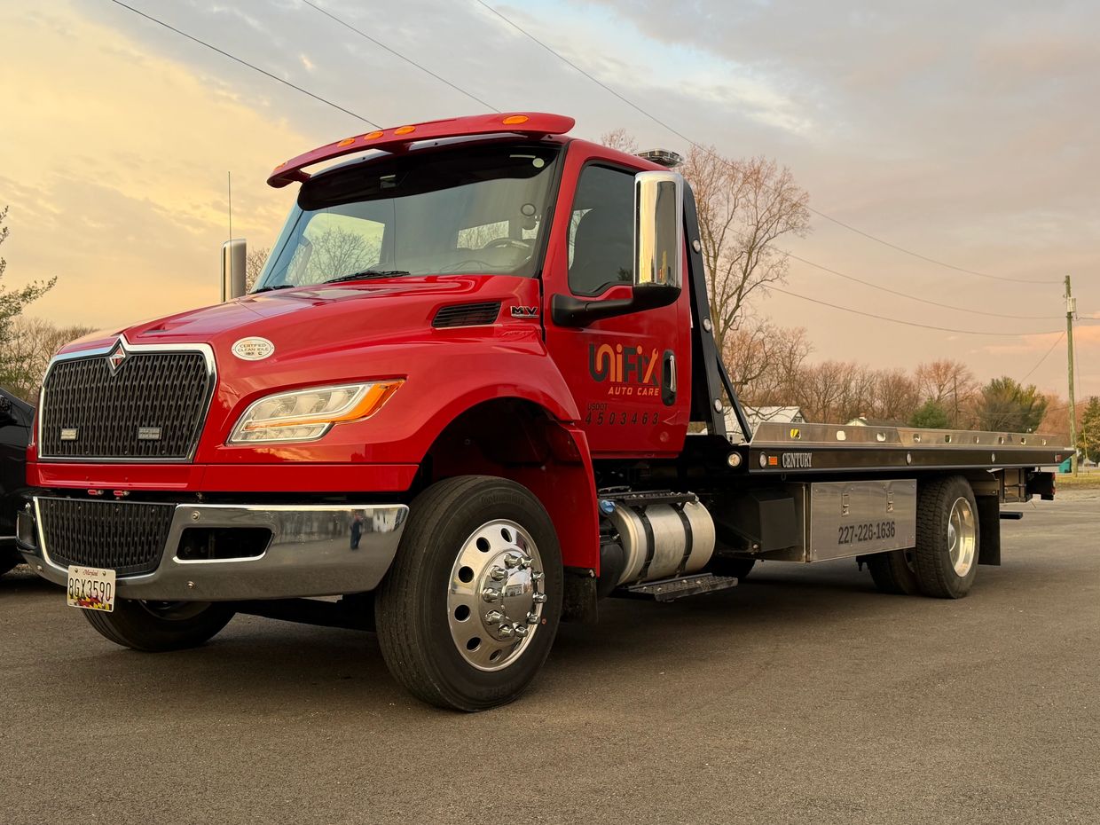 Red tow truck parked on asphalt at sunset.