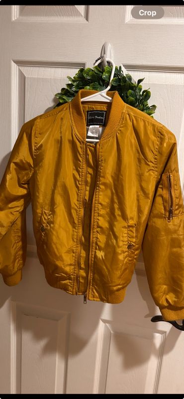 Mustard yellow bomber jacket hanging on a white door.