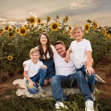 A happy family of four sitting in a sunflower field during sunset.