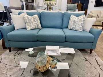 Modern teal sofa with patterned and plain cushions in a showroom setting.