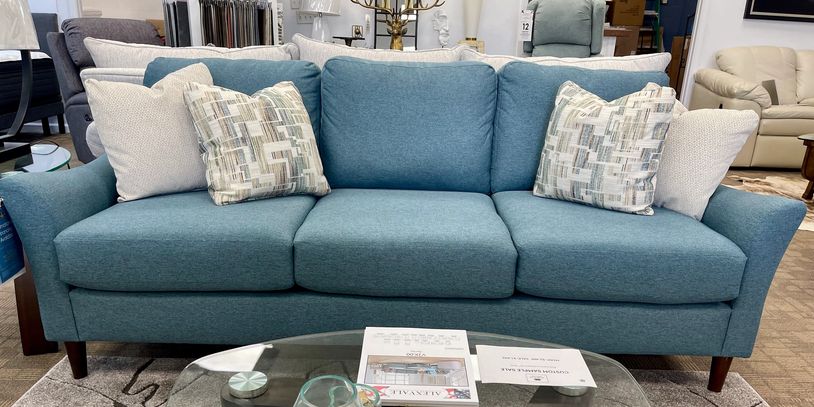 Modern teal sofa with patterned and plain cushions in a showroom setting.