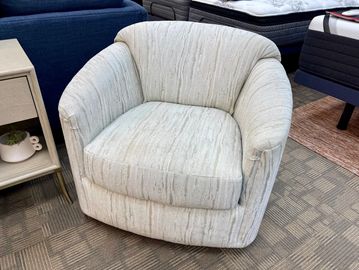Plush light beige armchair with subtle textured pattern in a showroom setting.