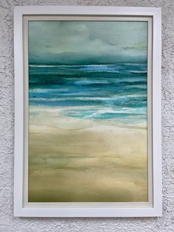 Framed watercolor painting of a serene beach and ocean under a cloudy sky.