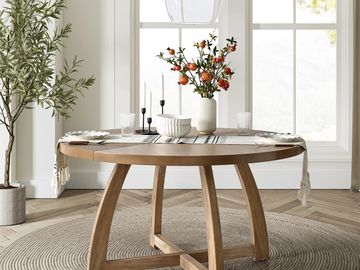 Round wooden dining table with a vase of pomegranates and candles.