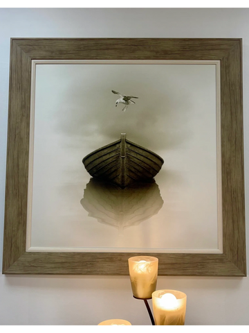 Framed photo of a boat and a bird, lit by candles below.