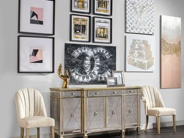 Elegant living room setup with beige chairs, a gold-accented sideboard, and luxury brand artwork on the wall.