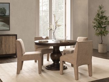 Cozy dining area with a round wooden table and upholstered beige chairs in a softly lit room.