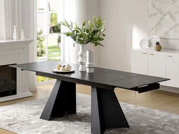 Modern black dining table with geometric legs and decorative vases in a bright, elegant room.