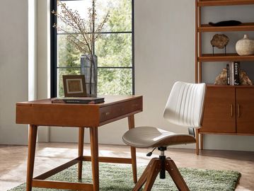 A mid-century wooden desk and chair set in a bright, minimalist room.