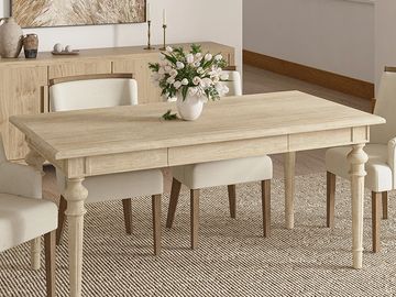 Elegant wooden dining table with beige cushioned chairs and floral centerpiece in a bright room.